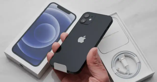 Czarny iPhone w ręce, obok pudełko z telefonem i kablem.