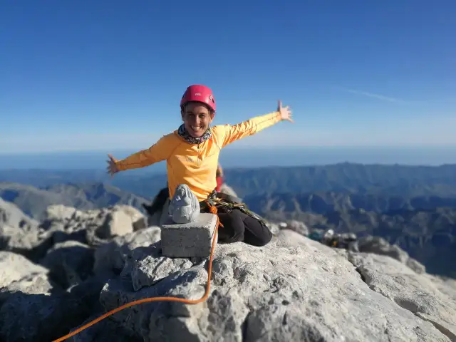 Szczęśliwa alpinistka na szczycie góry, z widokiem na pasmo górskie. W tle widać morze. To szczyt Naranjo de Bulnes.