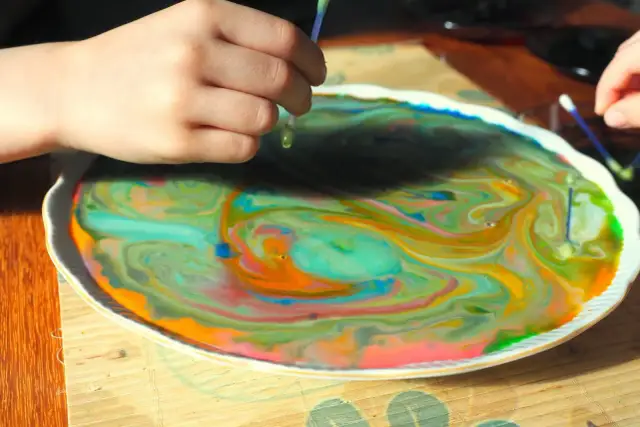 Dziecko dodaje barwniki do mleka, tworząc wirujące, kolorowe wzory.
