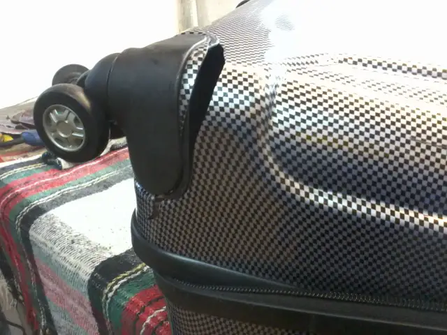 Uszkodzone kółko walizki na tle kratkowanego materiału.