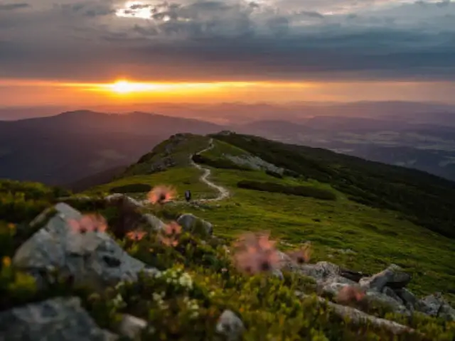 Zachód słońca nad pasmem górskim z krętą ścieżką i pojedynczym turystą.