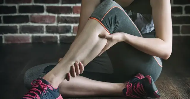 Kobieta masuje bolącą łydkę po intensywnym treningu. Czy zakwasy po treningu są dobre? To znak, że mięśnie pracują.