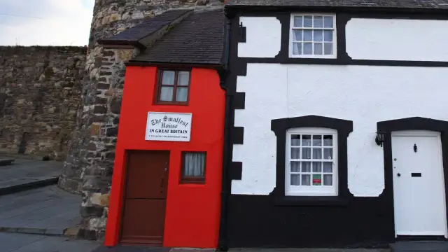 Najmniejszy dom na świecie, jaskrawoczerwony, obok białego domu z czarnymi zdobieniami.