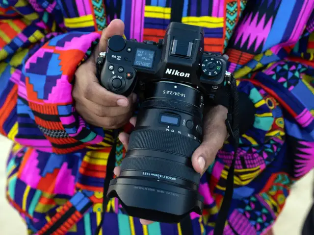 Osoba trzyma aparat Nikon Z z obiektywem na tle kolorowego ubrania.