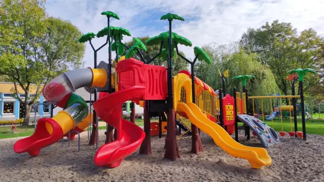 Kolorowy plac zabaw z zjeżdżalniami, drabinkami i huśtawkami na piasku.