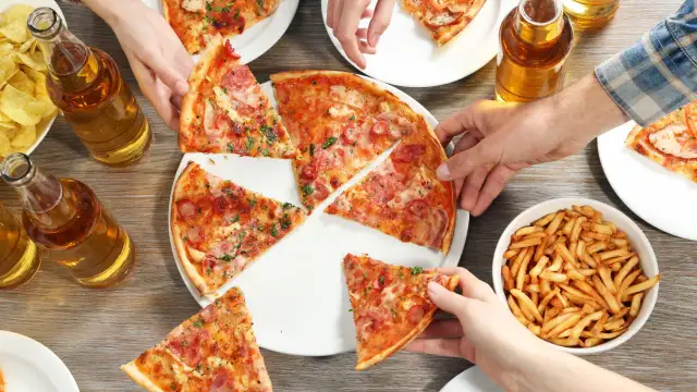Ręce sięgają po kawałki pizzy, frytki i butelki piwa.