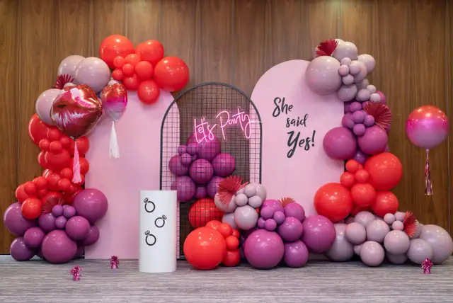 Girlanda z różowych i czerwonych balonów, neonowy napis "Let's Party" i napis "She said Yes!".