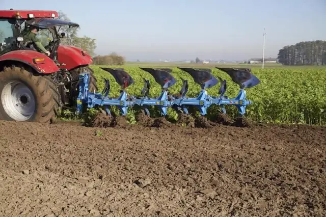 Czerwony traktor z pługiem orze pole.