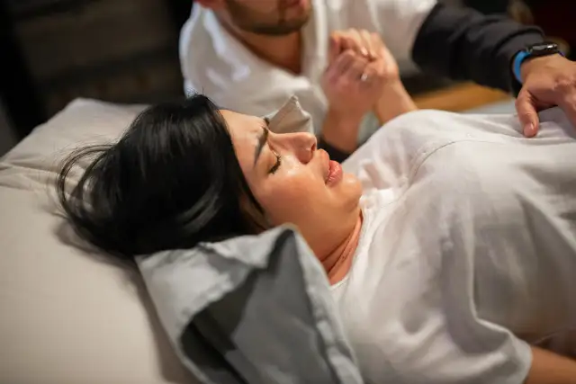 Mąż przy porodzie trzyma dłoń rodzącej kobiety, wspierając ją w tym ważnym momencie.