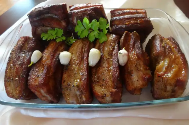 Pyszne żeberka w miodzie, pieczone z czosnkiem i natką pietruszki, prezentują się apetycznie na szklanej tacy.