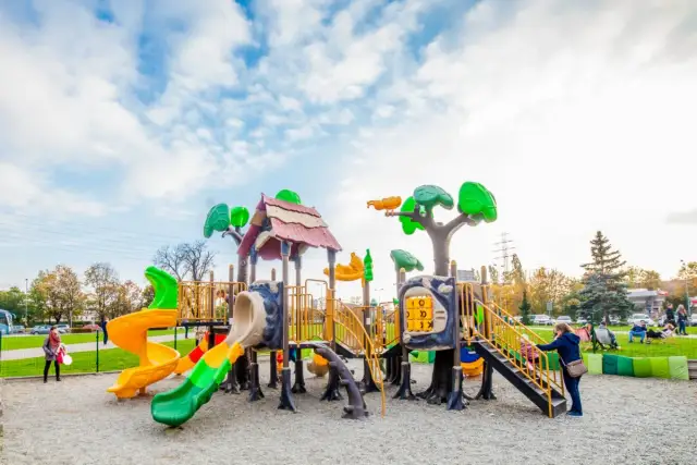 Kolorowy plac zabaw z wieloma zjeżdżalniami i elementami do wspinaczki, pod błękitnym niebem.