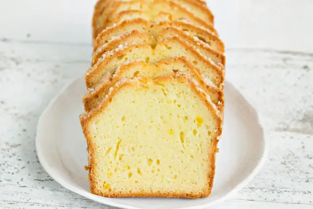Pokrojona babka piaskowa cytrynowa z cukrową posypką, ułożona na białym talerzu.