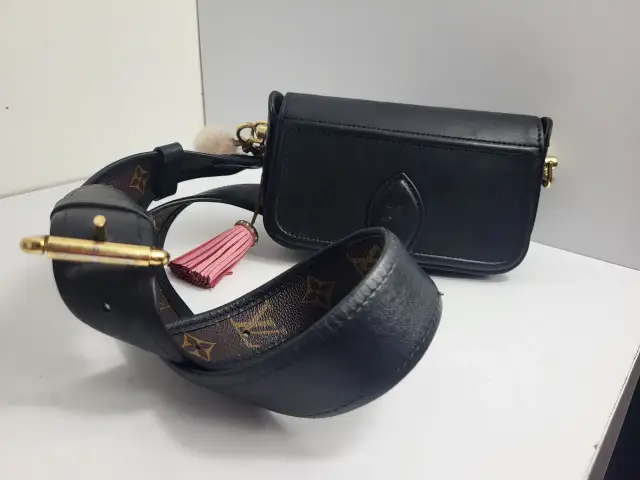 Elegancka, czarna louis vuitton torebka z ozdobnym, różowym pomponem i paskiem z monogramem.