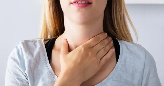 Kobieta dotyka gardła, zastanawiając się, tsh co to za badanie.