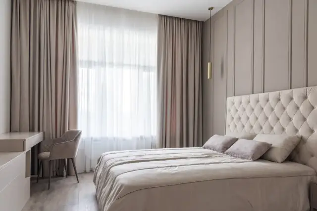 Elegancka sypialnia z dużym łóżkiem i zasłonami, które mogą być zawieszone na karniszach lub szynach.