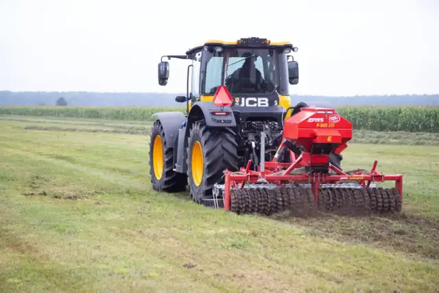 Ciągnik JCB z rozsiewaczem nawozu na polu.