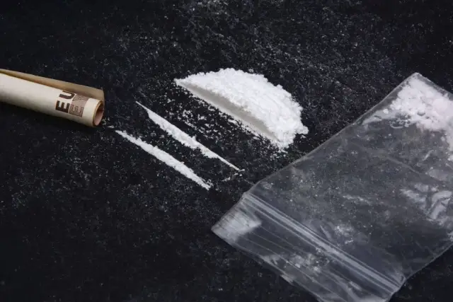 Proszek narkotykowy, zwinięty banknot euro i plastikowa torebka na czarnym tle.