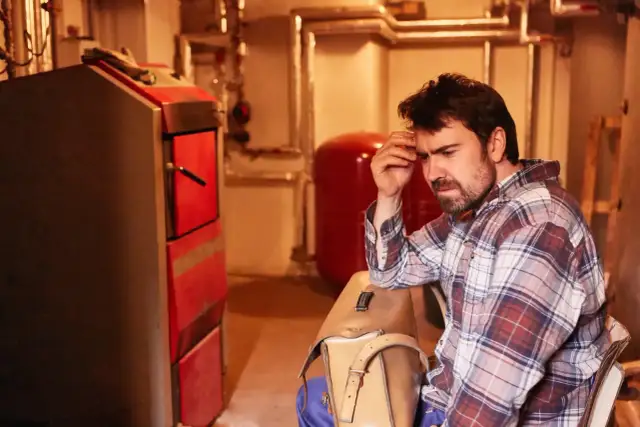 Zamyślony mężczyzna w kratę obok pieca. Zastanawia się, ile bierze hydraulik za podłączenie pieca.