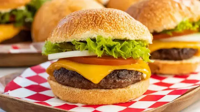 Soczysty burger z serem, sałatą, pomidorem i cebulą na czerwono-białej kratce.