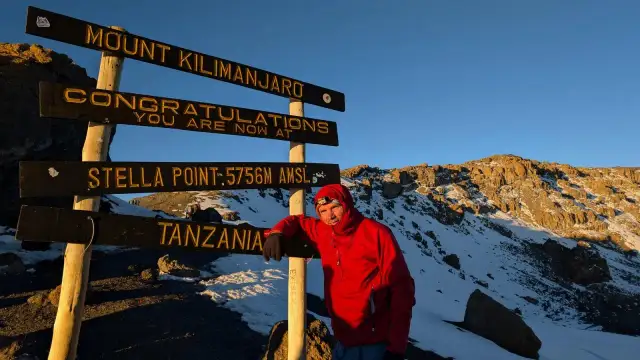Mężczyzna w czerwonej kurtce przy znaku "Mount Kilimanjaro, Stella Point". To właśnie tutaj jest Kilimandżaro!