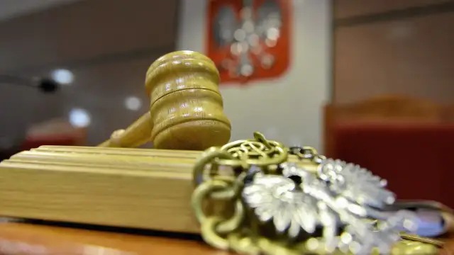 Młotek sędziowski i łańcuch z orłem na tle godła Polski.