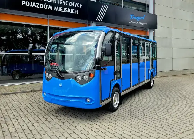 Niebieski bus elektryczny z logo Frugal na tle budynku z napisem "POJAZDÓW MIEJSKICH".