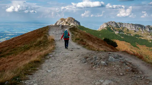 Szlak na czerwone wierchy z Kuźnic. Turystka z plecakiem idzie kamienistą ścieżką wśród traw.