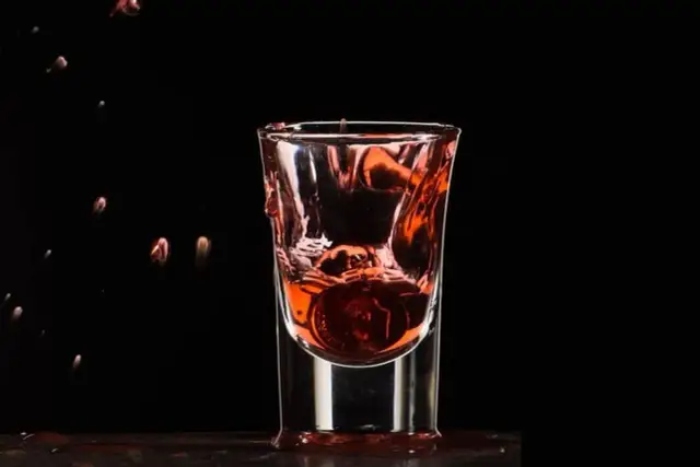 Wściekły pies drink, moneta spada do kieliszka z czerwonym płynem, tworząc fontannę.