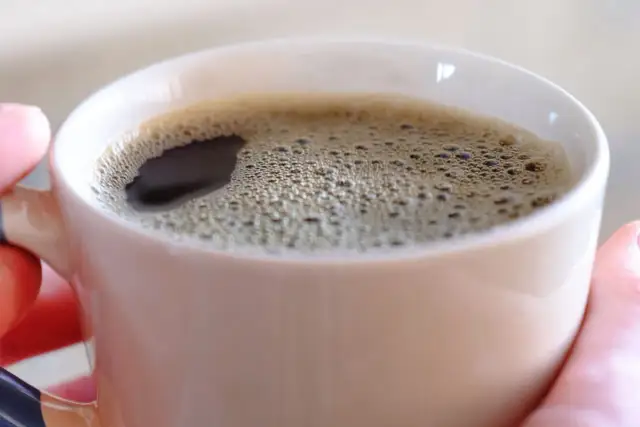 Gorąca kawa w kubku, która pobudza, bo tak działa kofeina. Piana na powierzchni świadczy o świeżości napoju.