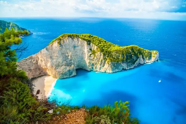 Widok na zatokę Navagio na Zakynthos z klifem, piaszczystą plażą i turkusową wodą.