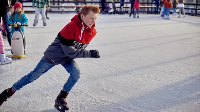 Chłopiec w kurtce i dżinsach śmiga na łyżwach po lodowisku. To jego ulubiona dyscyplina sportowa na lodzie.