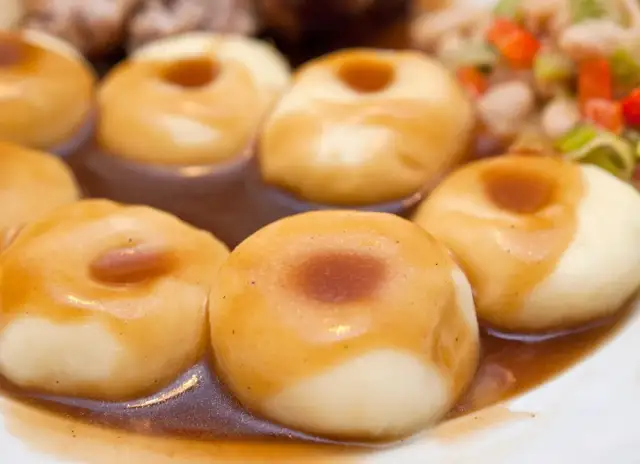 Kluski śląskie polane sosem, na talerzu z dodatkami.