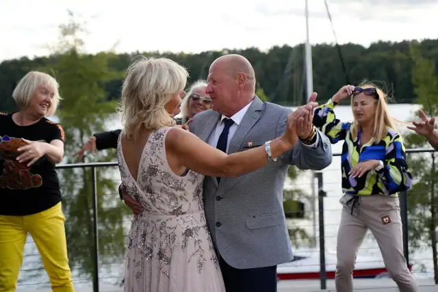 Para z Sanatorium Miłości tańczy przy jeziorze, podczas gdy inni uczestnicy bawią się w tle.