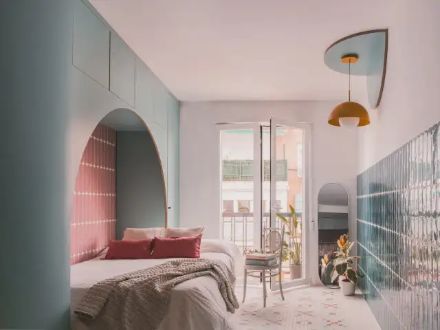 Nowoczesna aranżacja mieszkania 50m2 w bloku: łóżko z łukiem i różowymi płytkami, zielone ściany, lustro i rośliny.