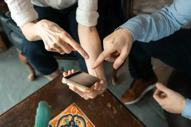 Dwie osoby wskazują palcami na ekran telefonu, dyskutując, ile kosztuje aplikacja.