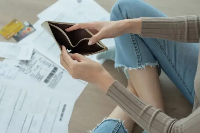 Kobieta z pustym portfelem siedzi wśród rachunków i kart kredytowych.