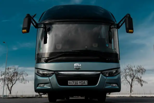 Przód jasnoniebieskiego autokaru z tablicą rejestracyjną 01710 YDA na tle błękitnego nieba.