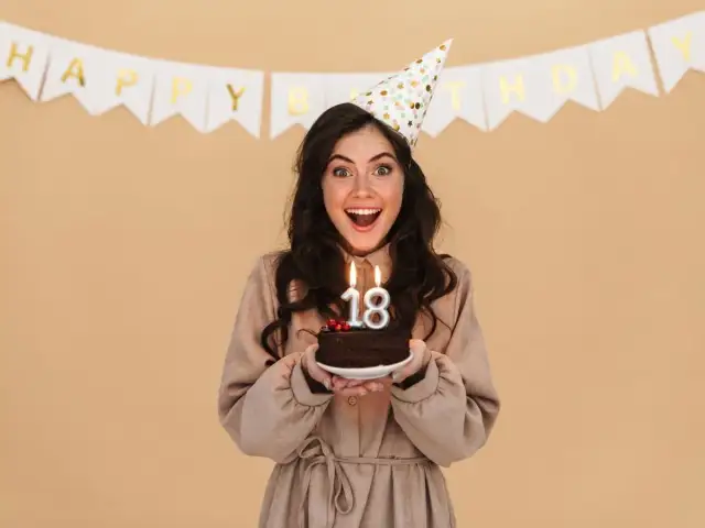 Radosna dziewczyna w czapce urodzinowej z tortem i świeczkami "18". Idealny prezent dla chrześniaka na osiemnastkę!