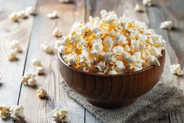 Drewniana miska pełna karmelowego popcornu na drewnianym tle.