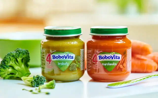 Dwa słoiczki BoboVita: brokuły i marchewka, idealne jako pierwsze pokarmy dla niemowląt po 4 miesiącu. Obok świeże warzywa.