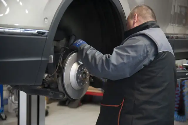 Mechanik sprawdza żywotność klocków hamulcowych przy tarczy hamulcowej samochodu na podnośniku.