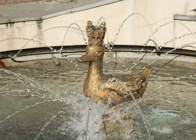 Złota kaczka w koronie, fontanna przypominająca legendę o złotej kaczce, tryska wodą.