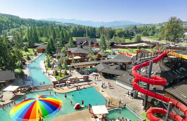 Widok z lotu ptaka na kompleks basenów termalnych z atrakcjami wodnymi, zjeżdżalniami i górami w tle.