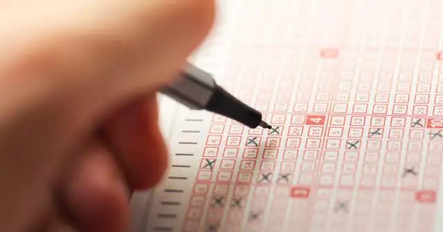 Dłoń z długopisem zaznacza liczby na kuponie Lotto.