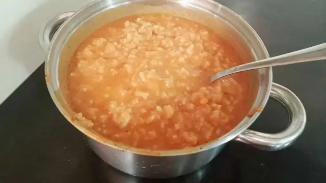 Gęsta zupa pomidorowa z ryżem w metalowym garnku, z widoczną łyżką.