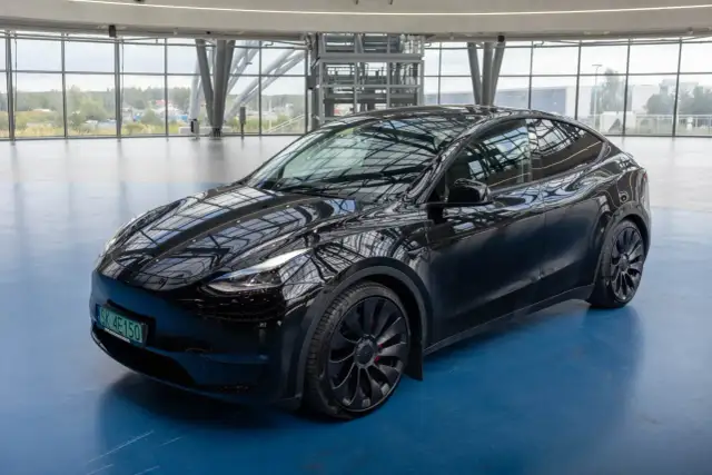 Czarny Tesla Model Y na niebieskiej podłodze, w nowoczesnym wnętrzu z dużymi oknami.