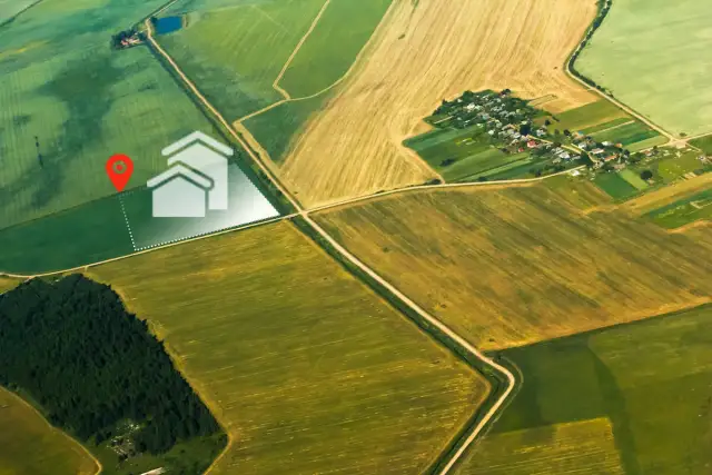 Działka rolna z warunkami zabudowy może stać się działką budowlaną. Widok z lotu ptaka na pola i wyznaczoną działkę z ikoną domu.