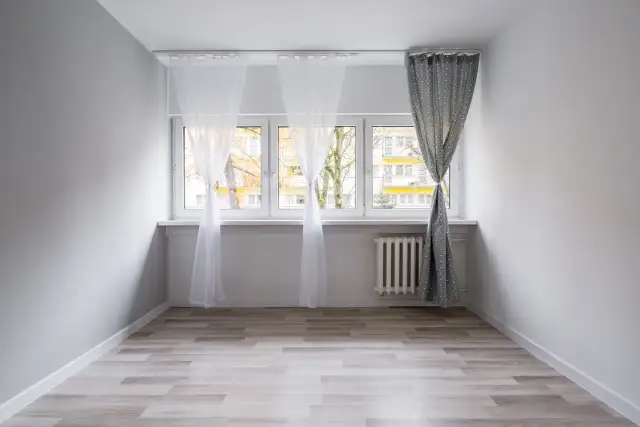 Biały karnisz sufitowy zamontowany nad oknem, na którym wiszą zwiewne firanki i zasłona.