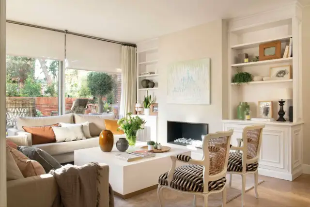 Salón moderno con sofá beige, mesa de centro blanca, chimenea y dos sillones con estampado de cebra.