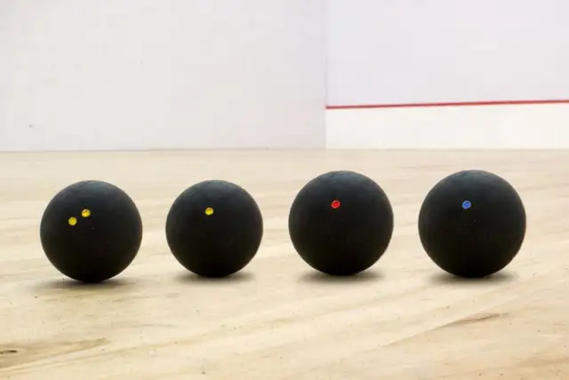 Cztery czarne piłki do squasha z kolorowymi kropkami na drewnianej podłodze.